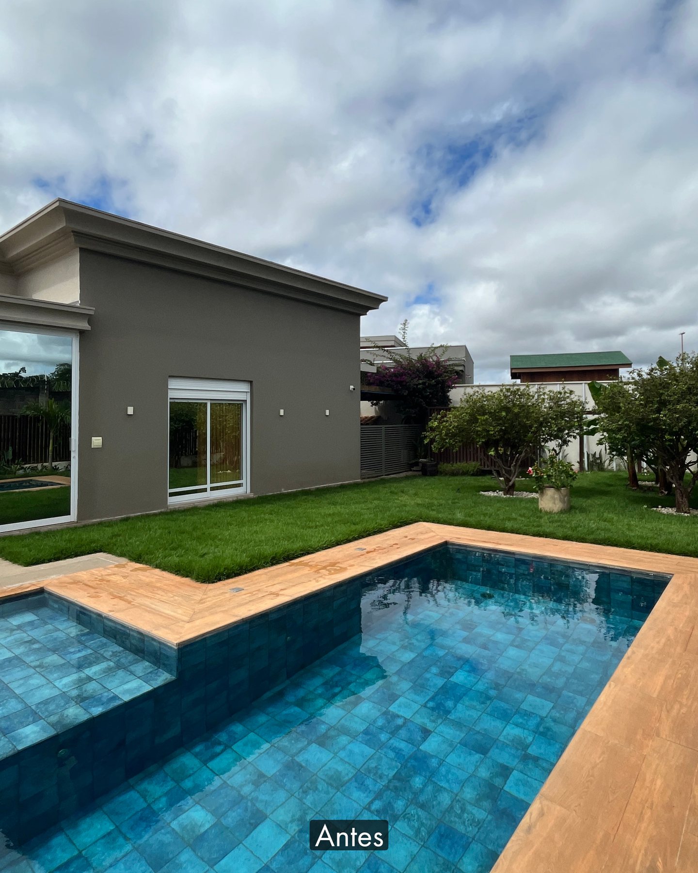 Área de piscina de residência antes da obra, com deck em porcelanato, gramado e a parede cega da casa ao fundo